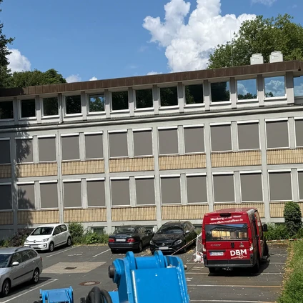 Fassade eines Gewerbegebäudes mit vielen Parkplätzen Autos und einem roten Service-Van
