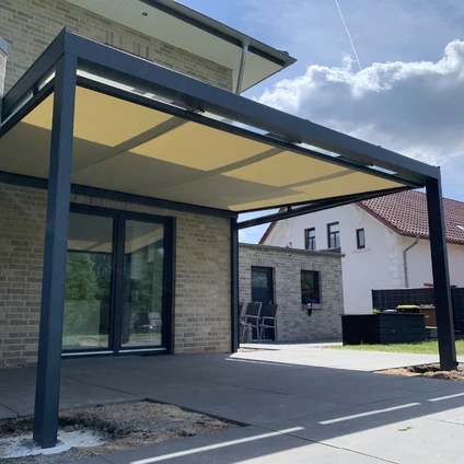 Moderne Überdachung mit schwarzem Rahmen und Sonnensegel über einem Haus mit Ziegelsteinfassade
