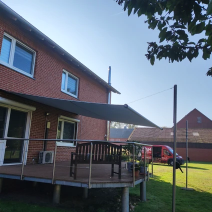 Familienhaus mit Holzdeck und Sonnenschirm aufgenommen an einem hellen Sommertag vor Grün