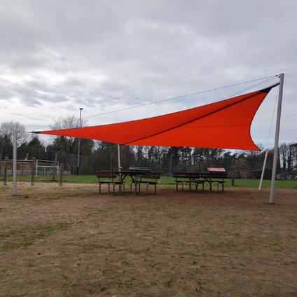 Orange Sonnensegel über Picknicktischen auf einer grasbewachsenen Fläche unter bewölktem Himmel