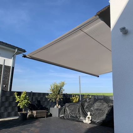 Sonnige Patio-Szene mit ausgefahrener beiger Markise und Pflanzen auf einem Pflasterboden unter blauem Himmel