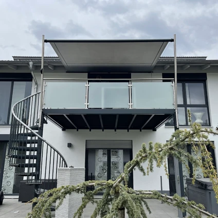 Modernes Wohnhaus mit schwarzer Wendeltreppe Balkon und grünem Laubwerk im Vordergrund