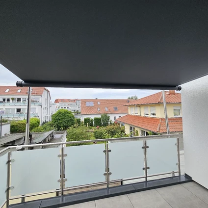Moderne Balkonansicht mit Glasgeländer das auf Wohnhausdächer und Grünblicke blickt