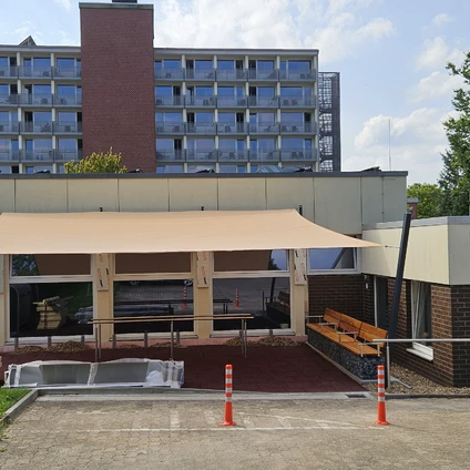 Modernes Gebäude mit hellem Vordach einer Terrasse und einem hohen Wohnhaus im Hintergrund