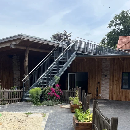Modernes Holzhaus mit Außentreppe Garten und begrünter Terrasse unter bewölktem Himmel