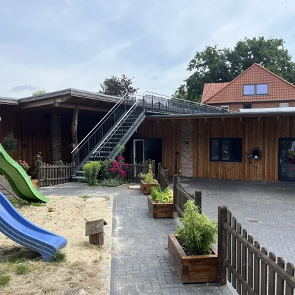 Modernes Holzhaus mit Außenaufgang Treppe und Kinderspielplatz im Vordergrund