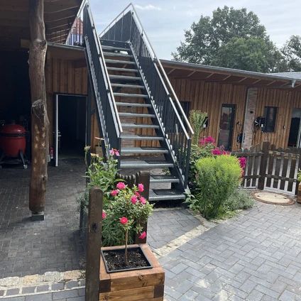 Moderne Metalltreppe an einem Holzhof umgeben von Blumenbeeten und Pflasterung