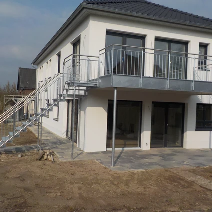 Modernes Wohnhaus mit Balkon und externer Metalltreppe auf einer Baustelle