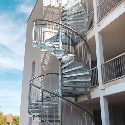 Geschwungene externe Spiraltreppe aus Edelstahl an der Fassade eines modernen weißen Wohngebäudes