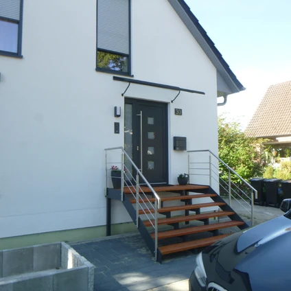 Moderne weiße Hausfassade mit großen Fenstern schwarzer Tür und auffälliger Außentreppe