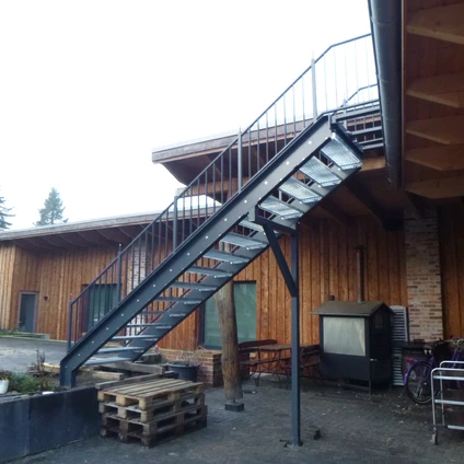 Metalltreppe zu einem modernen Holzhaus mit schwarzem Geländer und Treppenstufen