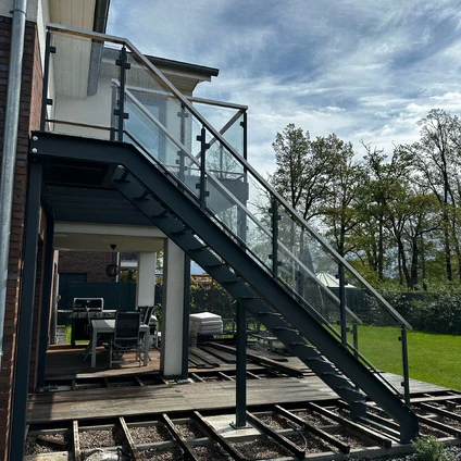 Moderne Außentreppe aus Stahl und Glasgeländern auf einem Holzdeck im Grünen