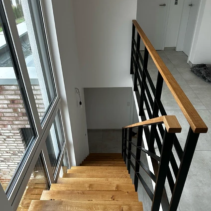 Moderne Holztreppe mit schwarzem Geländer und viel natürlichem Licht von großen Fenstern