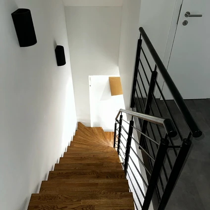 Moderne Holztreppe mit schwarzem Metallgeländer die in einen hellen minimalistischen Flur führt