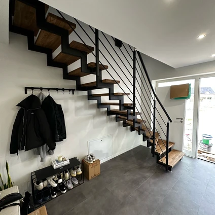 Minimalistisches Interieur mit offener Holztreppe und modernem schwarzem Metallgeländer