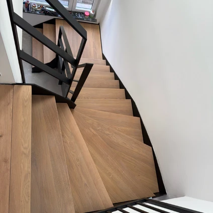 Moderne Holztreppe mit schwarzen Metallgeländern und weißen Wänden in einem hellen Interieur