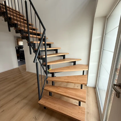 Moderne Treppe aus hellem Holz und schwarzem Metall mit freitragenden Stufen in einem hellen Wohnraum