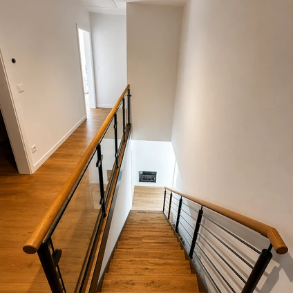 Modernes helles Treppenhaus mit Holzfußboden weißen Wänden und einem eleganten Geländer