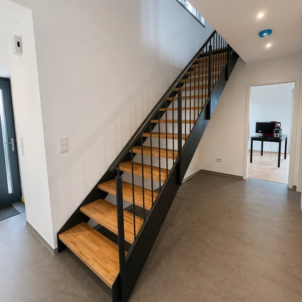 Moderne Treppe mit Holzstufen und schwarzen Geländern in einem hellen zeitgenössischen Flur