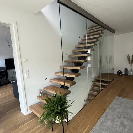 Moderne Holztreppe mit Glasgeländer in einem hellen Wohnbereich mit Holzboden