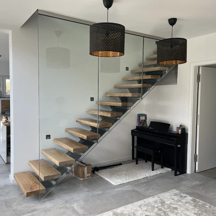 Moderne Treppe mit Glasgeländer dunklen Leuchten und schwarzem Klavier in einem hellen Interieur