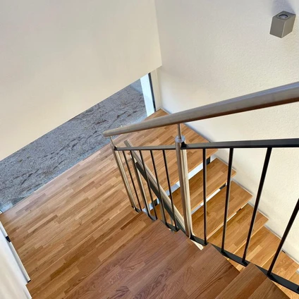 Moderne Holztreppe mit schwarzem Metallgeländer und einem silbernen Handlauf