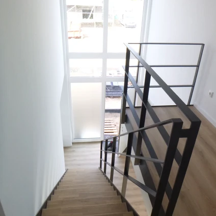 Moderne Holztreppe mit schwarzem Metallgeländer und viel Tageslicht ein minimalistisches Interieur