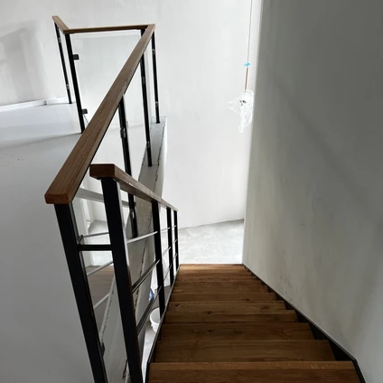 Holztreppe mit dunklem Geländer die in einen hellen Flur führt