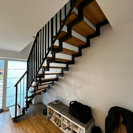 Moderne Holztreppe mit schwarzem Geländer und integrierter Sitzbank im hellen Wohn- und Eingangsbereich