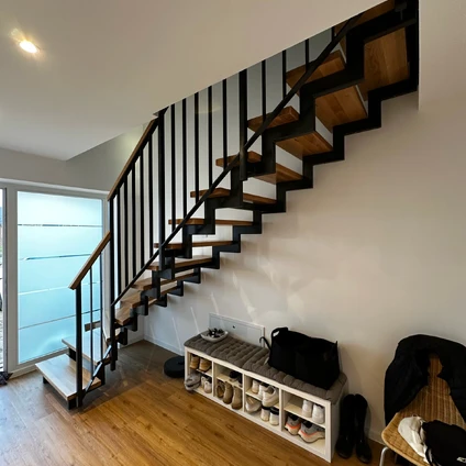 Moderne Treppe mit freitragenden Holzstufen schwarzem Geländer und Regal unter dem Treppenaufgang