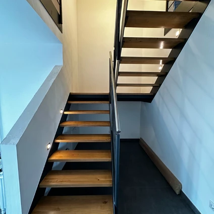 Moderne Holztreppe mit minimalistischem Design weißer Wand und dunklem Bodenbelag in einem Wohnhaus