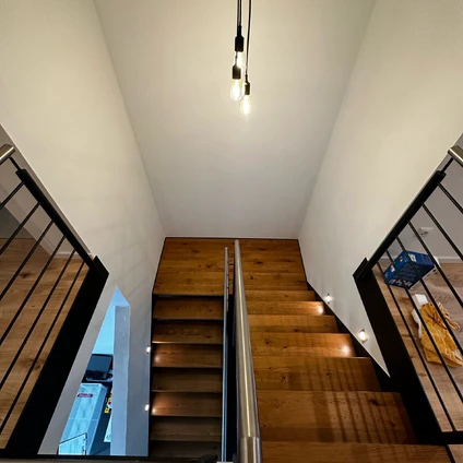 Elegante Holztreppe mit schwarzen Geländern in einem hellen modernen Interieur mit Deckenbeleuchtung