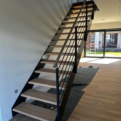 Moderne Treppe mit Holzstufen und schwarzem Metallgeländer in hellem Wohnraum mit Holzboden