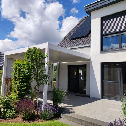 Modernes Zuhause mit weißem Eingangsbereich grauen Dach und viel Grün vor blauem Himmel