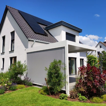 Modernes Haus mit Solarmodul-Dach und weißer Fassade umgeben von grünem Rasen und Blumen