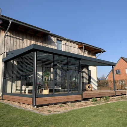 Moderner Glaspavillon an einem Holzhause mit Außenterrasse bei blauem Himmel