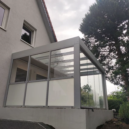 Modernes Glasdach-Wintergarten-Anbau an einem Haus mit grauem Rahmen und Vorhängen