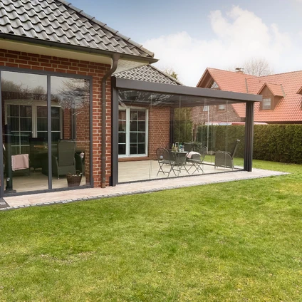 Moderne Glas-Terrassenüberdachung an Backsteinhaus mit Sitzgruppe im sonnigen Garten