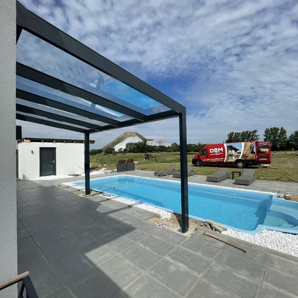 Moderner Pool mit schwarzem Überdachungsrahmen auf einer grauen Terrasse unter blauem Himmel