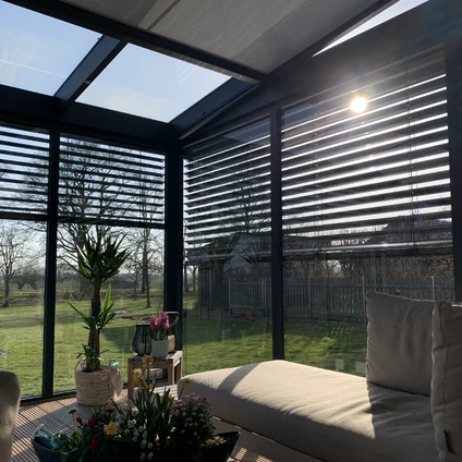 Modernes sonniges Solarium mit Sofa Pflanzen und Blick auf eine grüne ländliche Landschaft