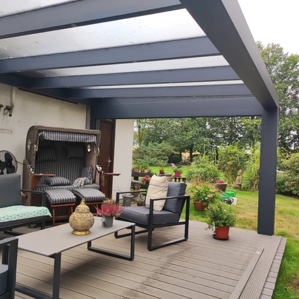 Outdoor-Lounge auf Holzterrasse unter dunkler Pergola mit Gartenblick und modernen Möbeln