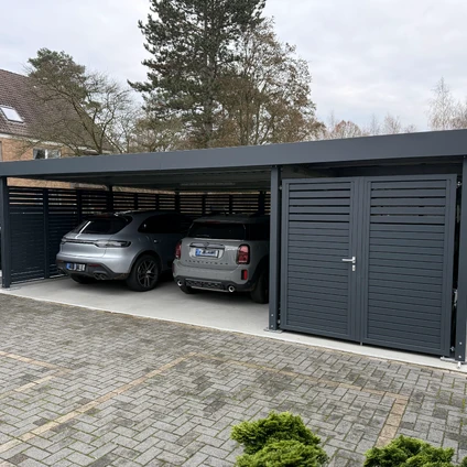 Modernes Carport mit zwei Autos auf einem gepflasterten Vorhof vor Wohnhäusern
