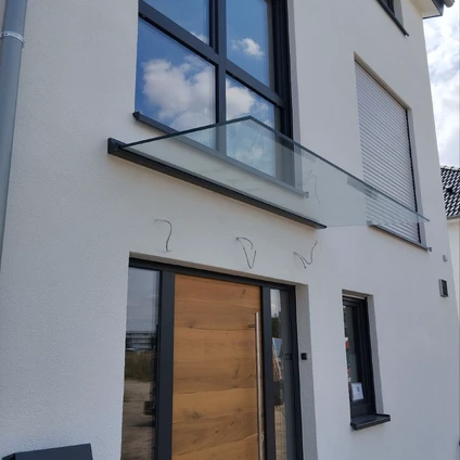 Moderne Fassade eines Hauses mit Holzhaustür großen Fenstern Glasgeländer und blauem Himmel