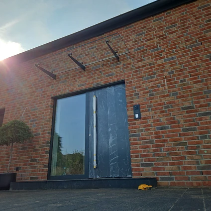 Rote Ziegelmauer mit modernem Fenster und oberhalb montierten schwarzen Außenleuchten bei Sonnenschein
